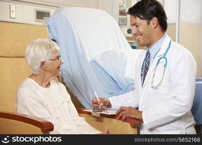 Doctor Taking Notes From Senior Female Patient Seated In Chair By Hospital Bed