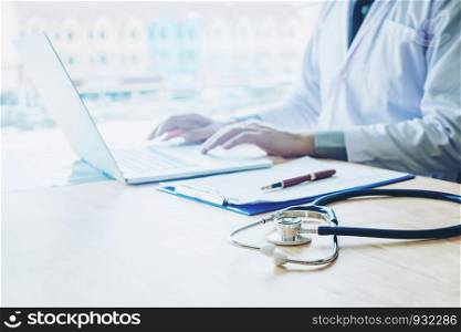Doctor typing information on Laptop in Hospital office focus on Stethoscope