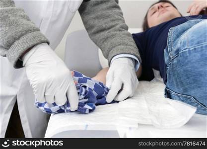 Doctor unwrapping a tea towel from the injured hand of a patient lying down on an examination table in the first aid room