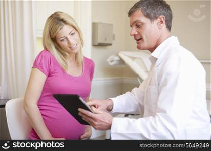 Doctor Using Digital Tablet In Meeting With Pregnant Woman