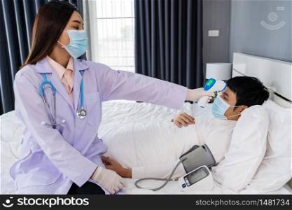 doctor using infrared forehead thermometer (thermometer gun) to measuring temperature of sick man in bed, people must be wearing medical mask protecting from coronavirus(covid-19) pandemic