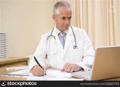 Doctor using laptop and writing in doctor&acute;s office