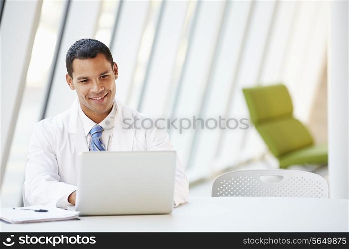 Doctor Using Laptop Sitting At Desk In Modern Hospital