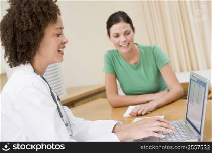 Doctor using laptop with woman in doctor&acute;s office smiling