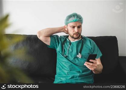 Doctor using phone in the resting room, wearing surgical gown. Doctor using phone in the resting room