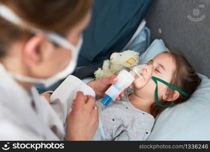 Doctor visiting little patient at home. Child having medical inhalation treatment with nebuliser. Girl with breathing mask on her face. Woman wearing uniform and face mask