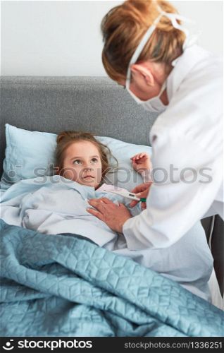 Doctor visiting little patient at home. Measuring the temperature of sick girl lying in bed. Woman wearing uniform and face mask. Medical treatment