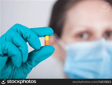 Doctor wearing blue face medical mask and green latex gloves holding tablet pill on grey hospital wall background. Antibiotics and virus treatment tablet.