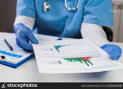 Doctor wearing protective gloves holding document chart,analyzing COVID-19 graph data,Coronavirus global pandemic outbreak crisis,stats showing number of infected patients,death toll,mortality rate