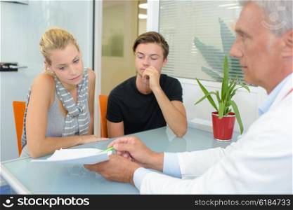 Doctor with couple, pointing to paperwork