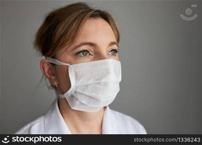 Doctor with face covered with mask. Portrait of young woman wearing the uniform and mask to avoid virus infection and to prevent the spread of disease. Real people, authentic situations