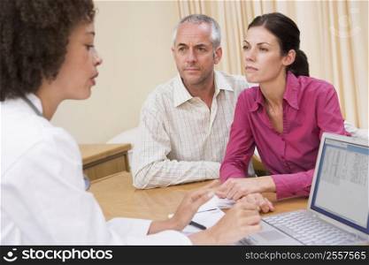 Doctor with laptop and couple in doctor&acute;s office frowning