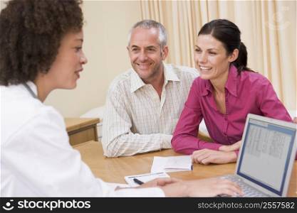 Doctor with laptop and couple in doctor&acute;s office smiling