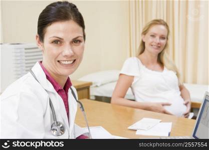 Doctor with laptop and pregnant woman in doctor&acute;s office smiling