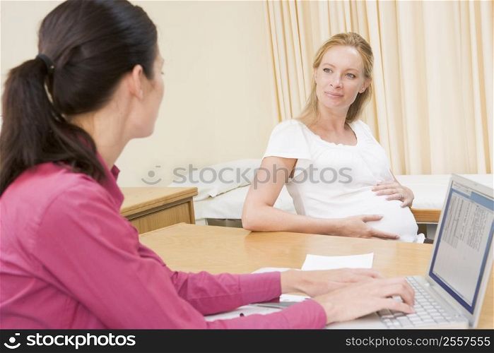 Doctor with laptop and pregnant woman in doctor&acute;s office smiling