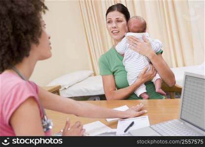 Doctor with laptop and woman in doctor&acute;s office holding baby