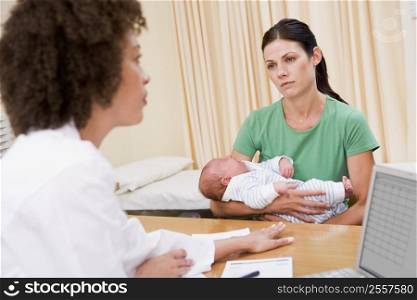 Doctor with laptop and woman in doctor&acute;s office holding baby