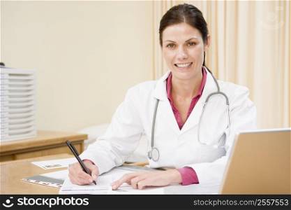 Doctor with laptop writing in doctor&acute;s office smiling
