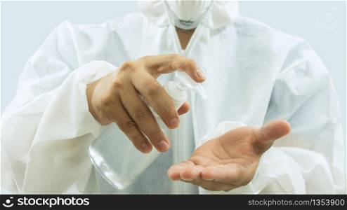 Doctor with mask and white bioprotective suit washing his hands with a bottle of alcohol gel in the foreground on white background. Doctor with mask and bioprotective suit washing his hands with a bottle of alcohol gel in the foreground on white background