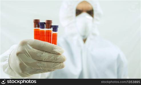 Doctor with mask and white bioprotective suit with arm extended forward and his right hand holding 4 test tubes with blood sample in the foreground on white background. Doctor with mask and bioprotective suit with arm extended forward and his right hand holding 4 test tubes with blood sample in the foreground on white background