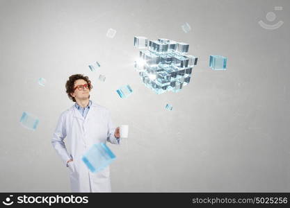 Doctor with mug in hand. Young doctor in glasses looking on cube figure