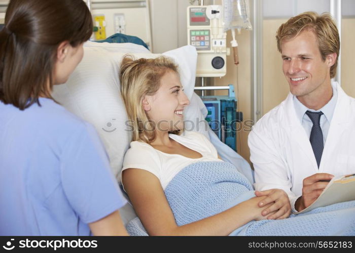 Doctor With Nurse Talking To Teenage Female Patient In Bed