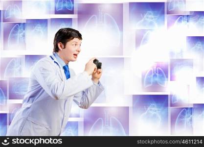 Doctor with photo camera. Young funny doctor taking photos with camera