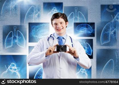 Doctor with photo camera. Young funny doctor taking photos with camera