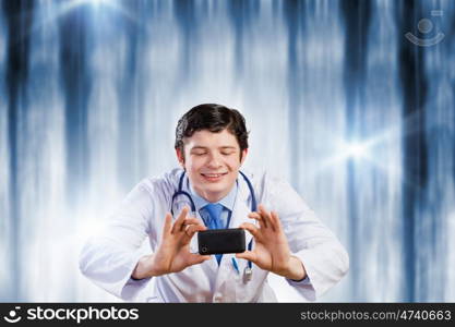 Doctor with photo camera. Young funny doctor taking photos with mobile phone camera