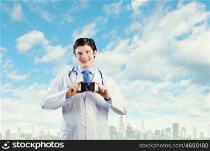 Doctor with photo camera. Young funny doctor taking photos with phone camera