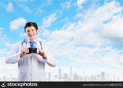 Doctor with photo camera. Young funny doctor taking photos with phone camera