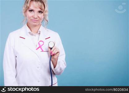 Doctor with pink cancer ribbon. Breast cancer. Medical help treatment concept. Female blonde doctor in white medic apron with pink ribbon holding stethoscope on blue background.