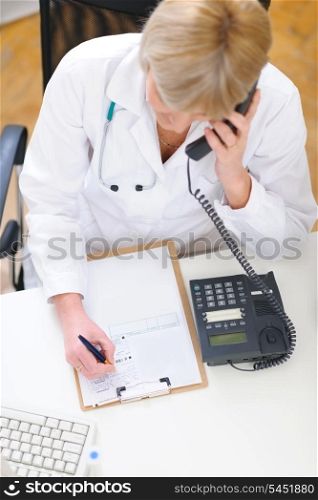 Doctor woman speaking phone and making notes in clipboard