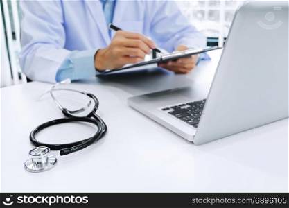 doctor working on laptop with stethoscope and paper clipboard, selective focus