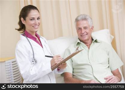 Doctor writing on clipboard while giving checkup to man in exam room smiling