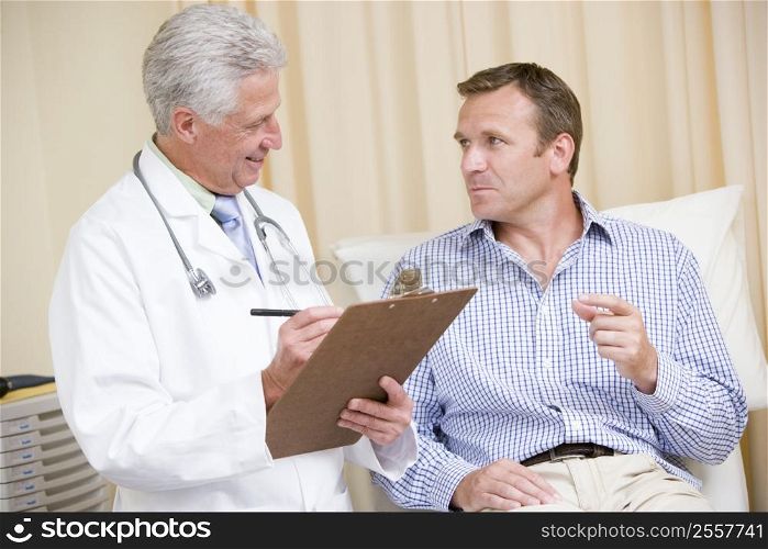 Doctor writing on clipboard while giving man checkup in exam room