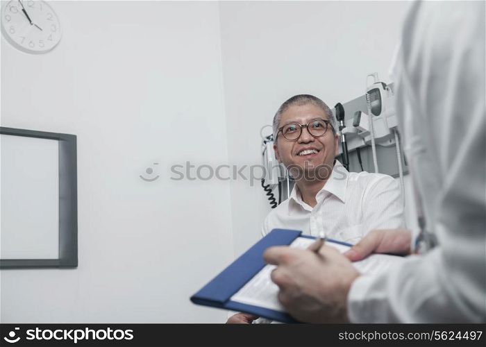 Doctor writing on medical chart with a smiling patient