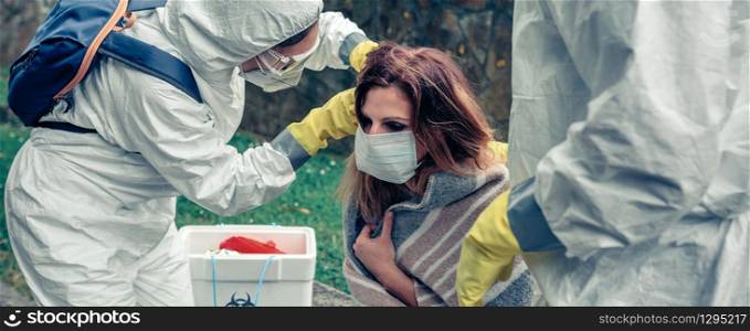 Doctors putting protective mask on woman infected by a virus outdoors