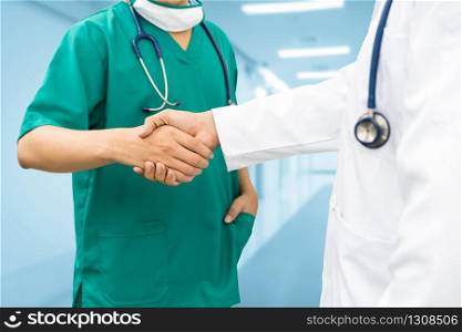 Doctors shaking hands with surgeon, standing in hospital background. Medical people teamwork and collaboration.