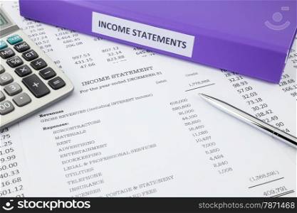 Document binder and income statement reports with detail list of revenues and expenses, pen pointing at credit revenues, concept for business accounting