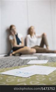 Documents on floor with tired businesswomen sitting in background