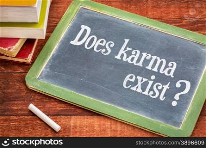 Does karma exist? A question in a white chalk on a vintage blackboard with a stack of books against rustic wooden table