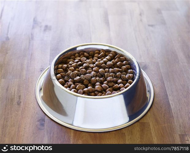 Dog dry food in the stainless steel bowl, wooden floor.