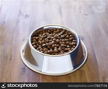 Dog dry food in the stainless steel bowl, wooden floor.