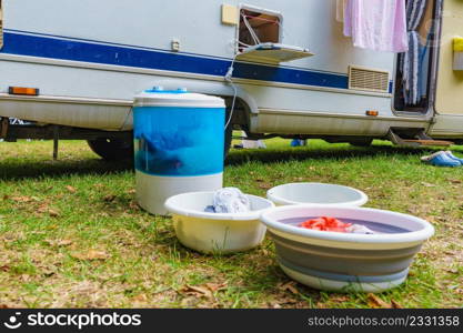 Doing laundry outdoor at caravan. Bowl with clean clothes and washing machine working. Camping on campground. Washing laundry outdoor at caravan