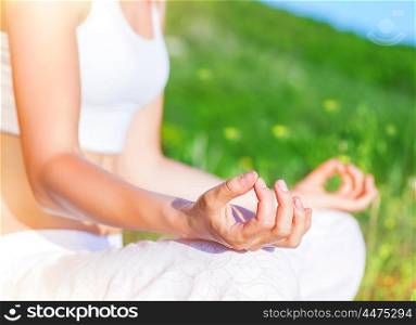 Doing yoga outdoors, woman sitting in the park in lotus pose and meditate, body part, soft focus, healthy lifestyle, finding harmony and soul balance