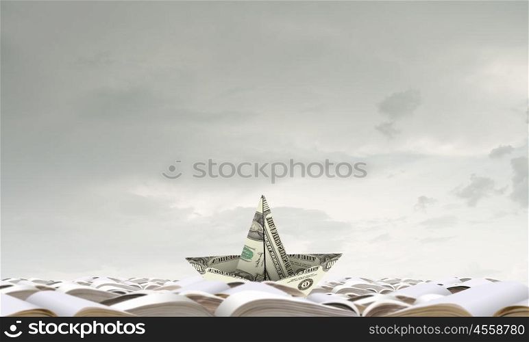 Dollar ship in water. Ship made of dollar banknote floating on pile of books