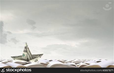 Dollar ship in water. Ship made of dollar banknote floating on pile of books