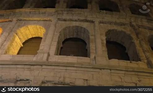 Dolly and low angle shot of famous Italian landmark - Coliseum. Ancient amphitheatre illuminated at night
