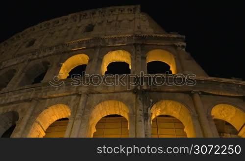 Dolly and low angle shot of illuminated Coliseum at night, the world famous ancient amphitheater in Rome, Italy